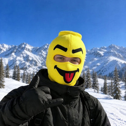 Blep yellow big head ski mask with a cheeky grin and red tongue out, worn on a snowy mountain