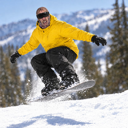 Snowboarder in a Goon Yellow jacket wearing the Cousin Wade ski mask, catching a small air off a roller on a sunny slope, worn with black ski goggles.