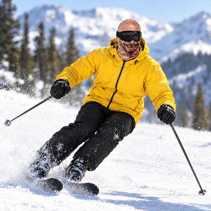 Skier in a Goon Yellow jacket wearing the Grandpa Gus ski mask, mid parallel carve, snow spraying off the skis on a sunny slope, worn with black ski goggles.